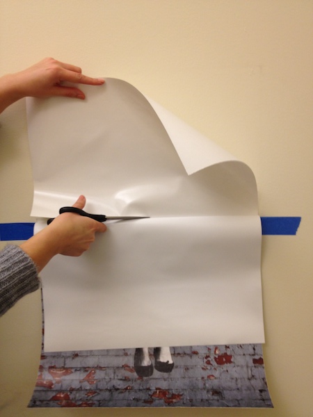 Photo a person using scissors to cut the excess backing paper off of a Wall Peel